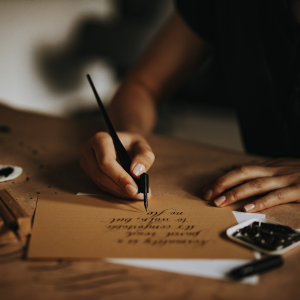 person writing a letter with old style ink pen on a desk with wax and seals