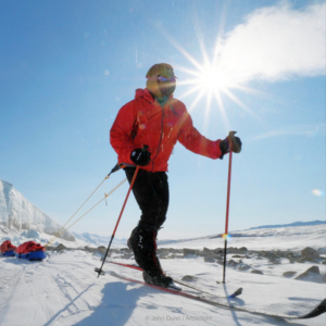 person on skiis wearing a red jacket against a background of snow, blue sky, and bright sun