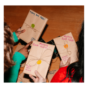 a group of people sitting around a table holding books wrapped in brown paper which have descriptions on the front