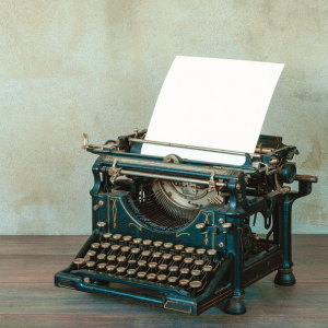 old-fashioned typewriter with paper sitting on a table with vintage style wall-paper in background