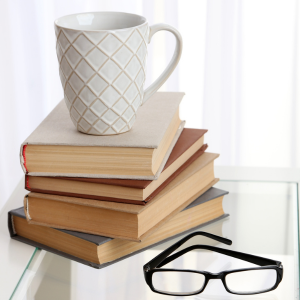 pile of books with white coffee mug and reading glasses