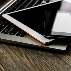 partial view of laptop keyboard with tablet and mobile phone on top